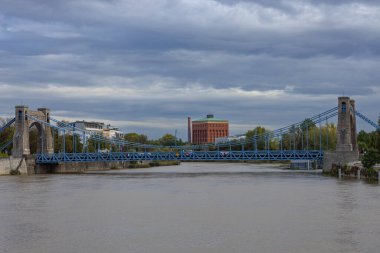 Sakin bir günde bulutlu gökyüzünün altında endüstriyel binalar inşa edilen tarihi mavi asma köprü. Kentsel mimari, ulaştırma altyapısı ve manzaralı şehir görüşleri kavramı