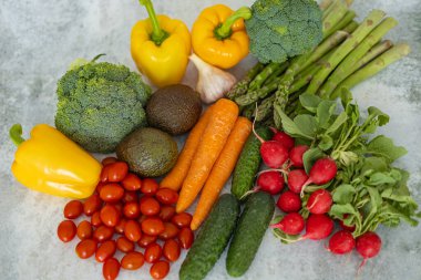 Brokoli, sarı dolma biber, kiraz domatesleri, havuç, salatalık, turp, kuşkonmaz, sarımsak ve avokado gibi taze organik sebzelerin açık arkaplan üzerindeki görüntüsü.