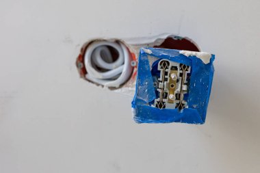 Koruyucu mavi bantla elektrik prizi kurulumunun yakın görüntüsü ve alçıpan panelinde açığa çıkan kablolar. Ev yenileme, elektrik işi ve inşaat güvenliği