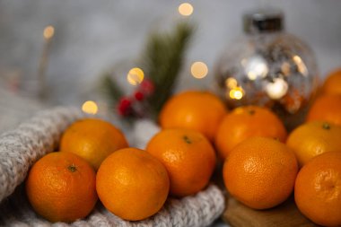Taze mandalinalar, arka planda şenlikli bokeh ışıkları ve Noel dekoru olan rahat yün bir battaniye. Kış tatilleri, mevsimlik meyveler ve şenlikli ev atmosferi