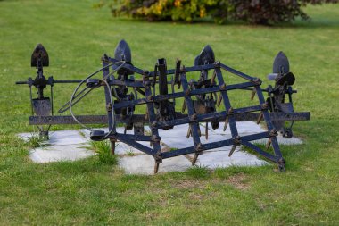 Vintage iron farming tool on display in green park on a sunny day. Concept of agriculture, historical equipment, and rural heritage clipart