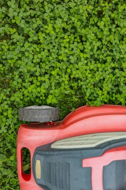 Red lawn mower on green clover field during lawn maintenance on a sunny day . Concept of garden care, landscaping and sustainable yard work clipart