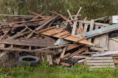 Kırsal bir alanda, fazla gelişmiş çimen ve bitki örtüsüyle çevrili ahşap enkaz ve hurda malzemeleri yığını. Atık yönetimi, geri dönüşüm ve çevre temizliği kavramı