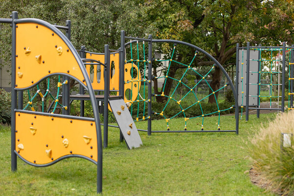 Современная открытая детская площадка с альпинистскими сооружениями и ярко-желтыми панелями в зеленом парке. Концепция активного образа жизни, отдыха на свежем воздухе и развития ребенка посредством физической активности