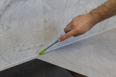 Mutfak tezgahı ile duvar arasındaki boşluğu mermer etkisiyle doldurmak için silikon dolgu aplikatörü kullanan bir işçi. Modern mutfaklar için ev yenileme, mühürleme süreci ve iç tasarım konsepti