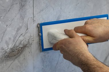 Profesyonel işçi, yenileme işlemi sırasında seramik fayans duvarına lastik şamandıra ile harç uyguluyor. Ev geliştirme, inşaat, döşeme, işçilik ve iç dekorasyon