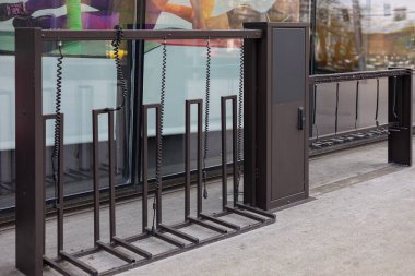 Modern kentsel elektrikli scooter şarj etme ve cam vitrinin yanında entegre kablo kilitleri olan bir otopark. Çevre taşımacılığı altyapısı, kentsel hareketlilik ve akıllı şehir teknolojisi