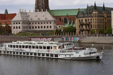 Wroclaw, Polonya-19 Nisan 2025: Oder Nehri üzerinde tarihi mimari ve katedralleri aşan manzaralı turist botu. Gezi turları, kültür mirası ve nehir kenti keşfi.