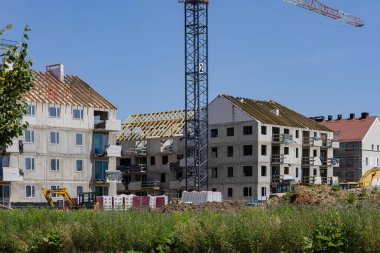 Güneşli bir günde vinçleri, iskelesi ve inşaat ekipmanları olan modern apartman binaları. Kentsel gelişim, gayrimenkul büyümesi ve inşaat mühendisliği