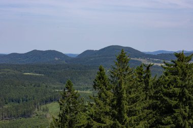 Güneşli yaz gününde açık mavi gökyüzünün altında yeşil orman tepeleri ve dağ sıralarının panoramik manzarası. Huzurlu doğa, yürüyüş turizmi, açık hava keşfi, kırsal kaçış ve ekolojik seyahat macerası