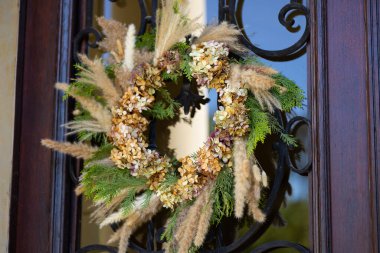 Kurumuş ortanca çiçeklerinden yapılmış sonbahar çelengi, kırsal ahşap kapıya asılmış pampa otları ve çam dalları. Konforlu mevsimlik ev dekorasyonu, kırsal atmosfer, klasik tarz ve el yapımı el işi.