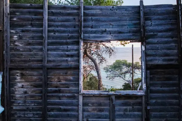 Paragkes Beach, Vouliagmeni, Atina 'da terk edilmiş bir barakanın harap olmuş ahşap duvarındaki kırık pencere çerçevesi.