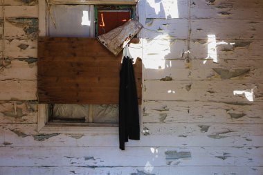 Tahta desenli duvarda boyası soyulan eski bir ahşap pencere kepengi.