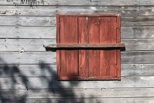 Yıpranmış ahşap bir pencere harap bir evin ahşap duvarında kırmızı bir kepenk.