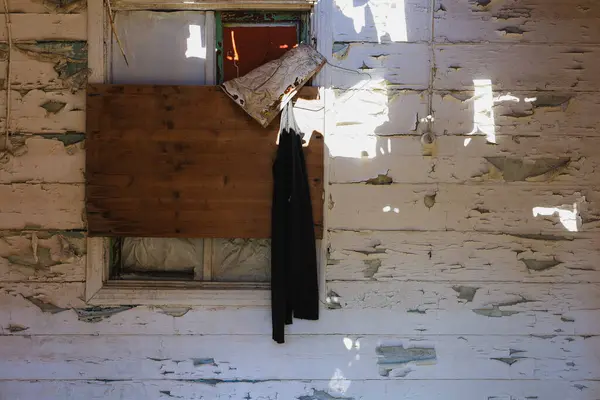 Tahta desenli duvarda boyası soyulan eski bir ahşap pencere kepengi.