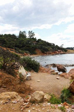 Paragkes Beach, Vouliagmeni 'deki Rugged Coastal Yolu' ndaki çalılıklardan sarkan çöplerle dolu plastik bir torba.