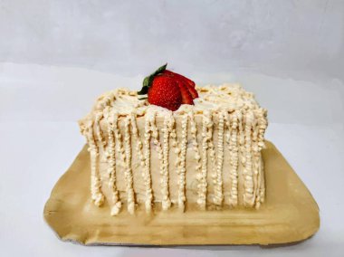 Dekoratif kremalı pasta açık renkli pasta tabanı üzerine tek bir taze çilekle süslenmiş. Kenarlarında özenle dekore edilmiş krema kenarları var..