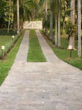 Uzun ağaçlar ve bahçe ışıklarıyla kaplı huzurlu bir patika, yemyeşil bir bahçeye kurulmuş büyüleyici beyaz ahşap bir kapıya götürür. Huzur ve sükunet hissi yayar..