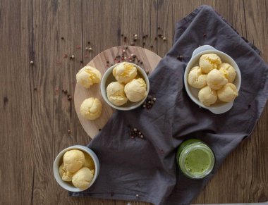 Geleneksel Brezilya peynirli ekmek ve ahşap masada yeşil meyve suyu. Üç kase peynirli ekmek ve bir bardak sağlıklı yeşil meyve suyu sanatsal olarak düzenlenmiştir..