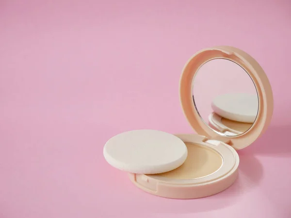 Face powder with sponge in beige case on pink background with copy space. Powder foundation, compact powder make-up.