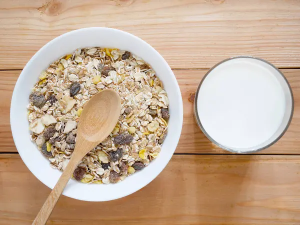 A Bowl of muesli breakfast and rolled oats with dried fruits and a glass of milk on wooden table. Top view.