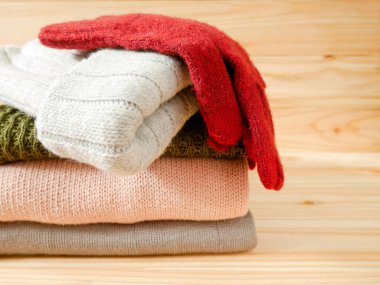Bir yığın süveter, örgü başlık ve ahşap arka planda örülmüş eldivenler. Kış giysileri kavramı.