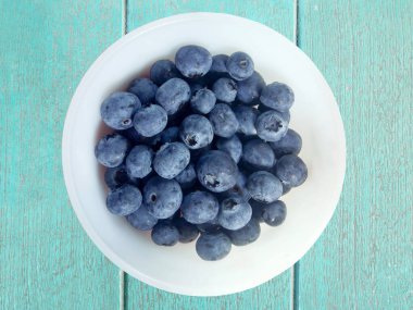 Tahta arka planda beyaz kasede taze yaban mersini.