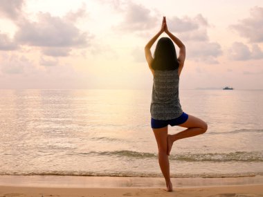 Gün batımında sakin plajda yoga yapan bir kadın.