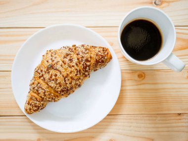 Tam tahıllı kruvasan ve ahşap masada bir fincan kahve. Üst görünüm.