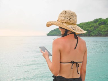 Sırtında güneş yanığı olan bir kadın sahilde cep telefonu kullanıyor.