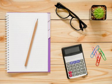 Kalem, hesap makinesi, bardaklar ve ataçlarla dolu boş bir defter. Üst görünüm.