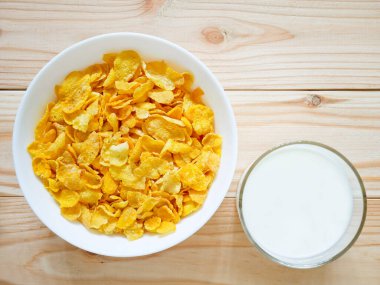 Altın mısır gevreği ve tahta masada bir bardak süt.