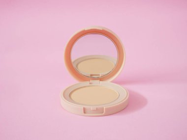 Pembe arka planda bej çantalı yüz pudrası. Pudra temeli, pudra makyajı..