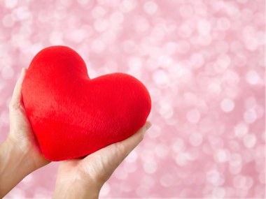 Pembe bokeh arka planda kırmızı kalbi tutan bir kadın.