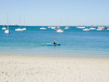Yatların arkasında kürek çeken bir adam.