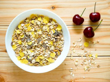 Bir kase müsli kahvaltısı, üzerine müsli dökülmüş kirazlar ve ahşap masa. Üst görünüm.