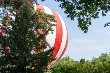 Kırmızı ve beyaz hava balonu ağaçların arkasında yerde.