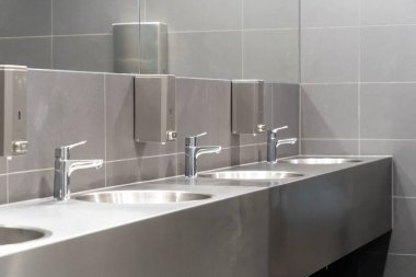 Gri fayanslı umumi tuvalette bir sıra metalik tuvalet.