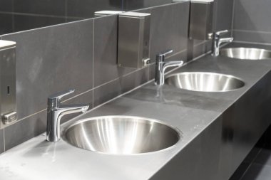Gri fayanslı umumi tuvalette bir sıra metalik tuvalet.
