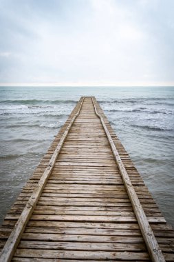 Adriyatik Denizi 'ne çıkan tahta iskele İtalya' da bulutlu bir sonbahar plajında.