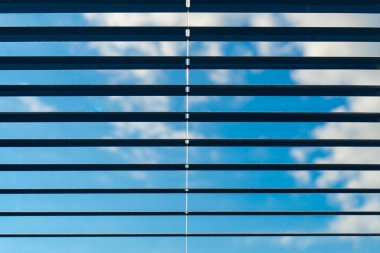 Half lowered window blinds in front of the blue sky clipart