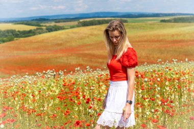 Kırmızı gelincik tarlasında kırmızı beyaz elbiseli sarışın genç bir kadın.