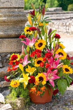 Arka planda eski taş duvarlı zambaklar ve güllerle renkli çiçek aranjmanı