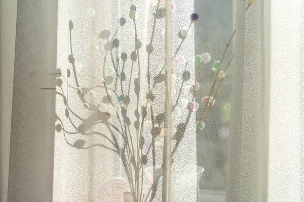 Perdelerden süzülen yumuşak güneş ışığıyla pencere kenarındaki Paskalya süslemesi.