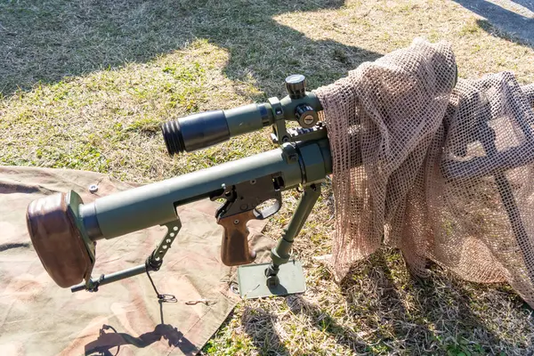 Büyük kalibreli kamuflajlı saldırı tüfeği kuru çimenlik alanda dürbünlü.