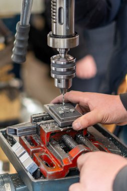 İşçi atölyede elle işletilen bir endüstriyel matkap kullanıyor.