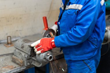 Mavi önlüklü işçi atölyede metal öğütüyor.