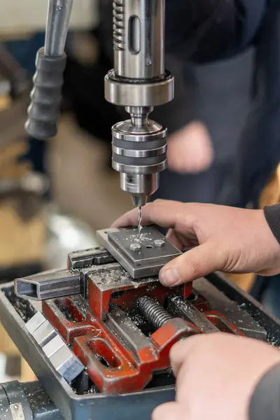 İşçi atölyede elle işletilen bir endüstriyel matkap kullanıyor.