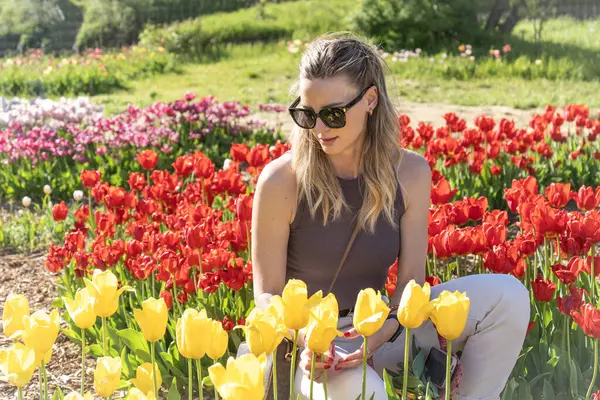 Güneş gözlüklü genç sarışın kadın renkli lale tarlasında oturuyor.