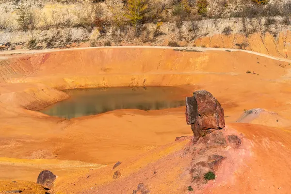 Terk edilmiş bir boksit madeninde parlak turuncu renklerle erozyona uğramış bir kayalık oluşumu.